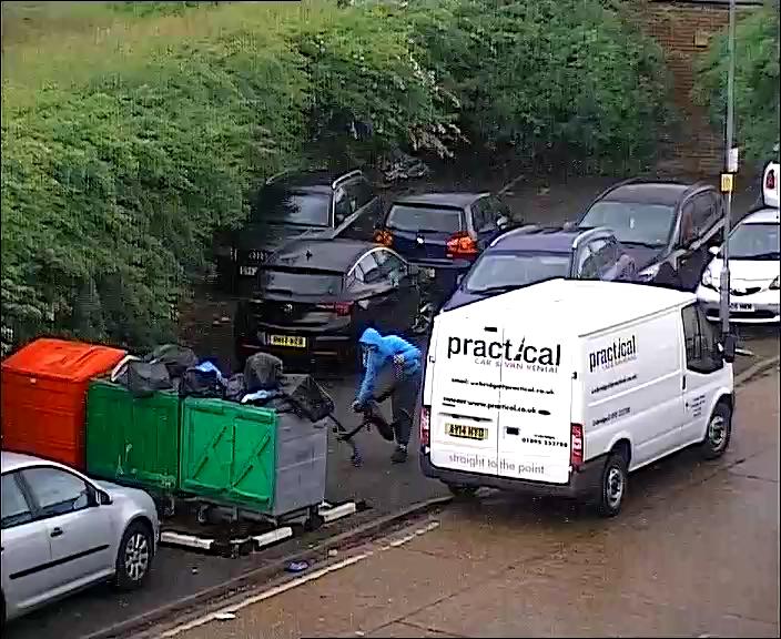 A white hire van pulled up at a communal rubbish area and a man taking a chair from van and fly-tipping it.