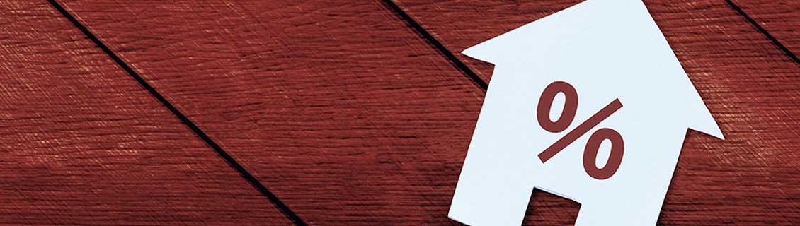 Close-up of small cut out of a house shape with the per cent symbol printed on it. House cut out is placed on a wooden surface.