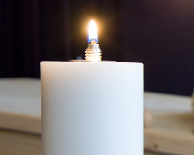 A burning candle with a coffin and a flower arrangement on the background in a mortuary
